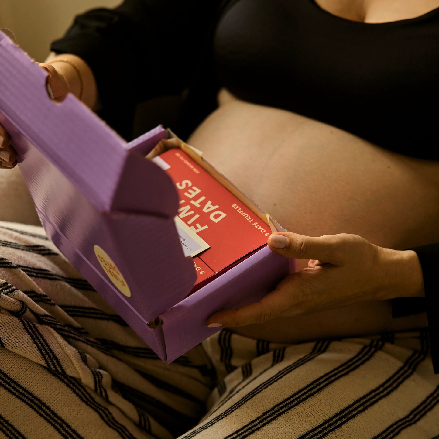 Person holding a purple shipping box with a box of final dates truffles, sitting on a couch.