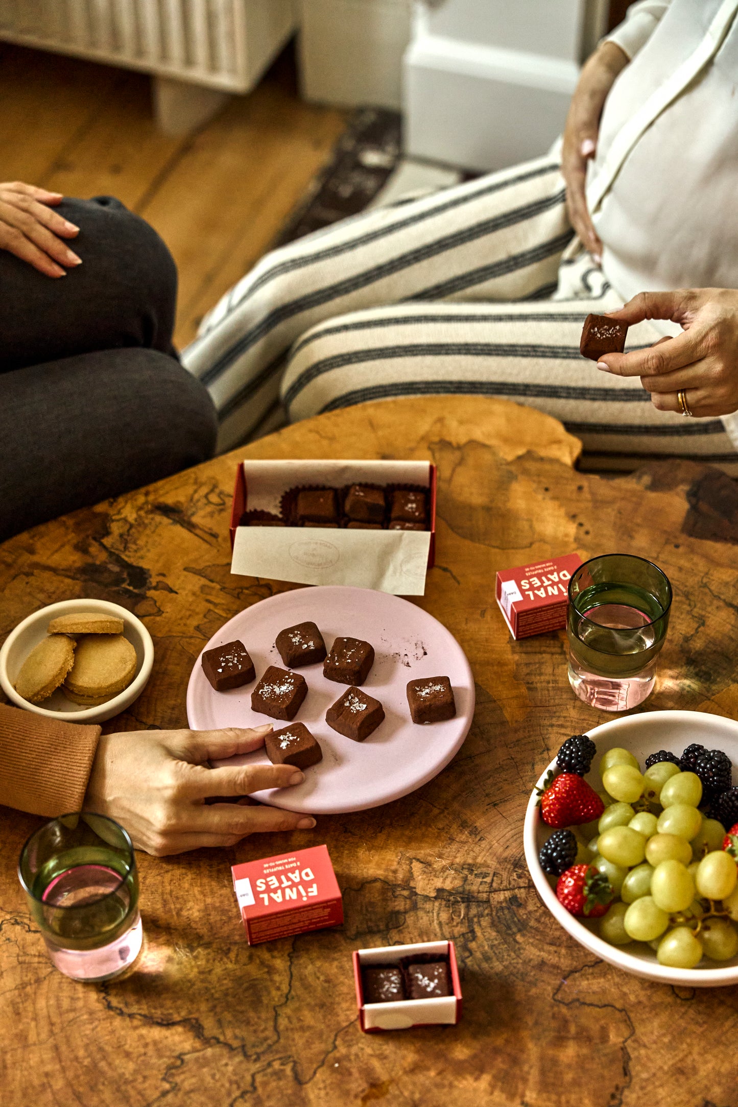People enjoying date chocolate truffles and fruit on a wooden table.